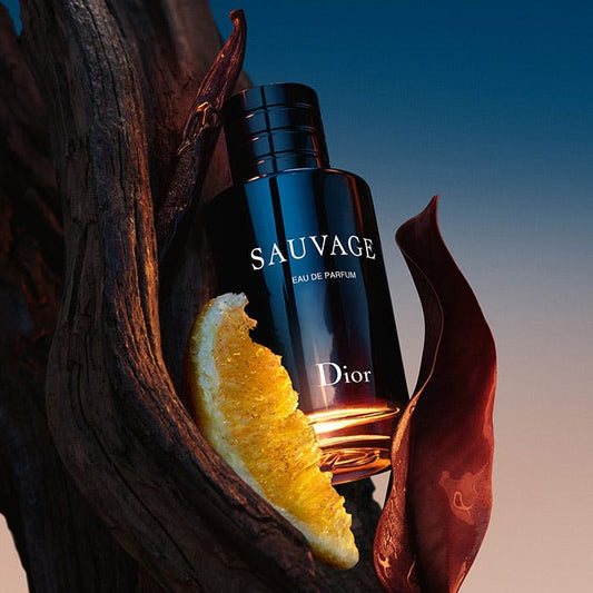 Dior Sauvage Eau de Parfum bottle with a slice of citrus on a wooden base against a gradient sunset backdrop.
